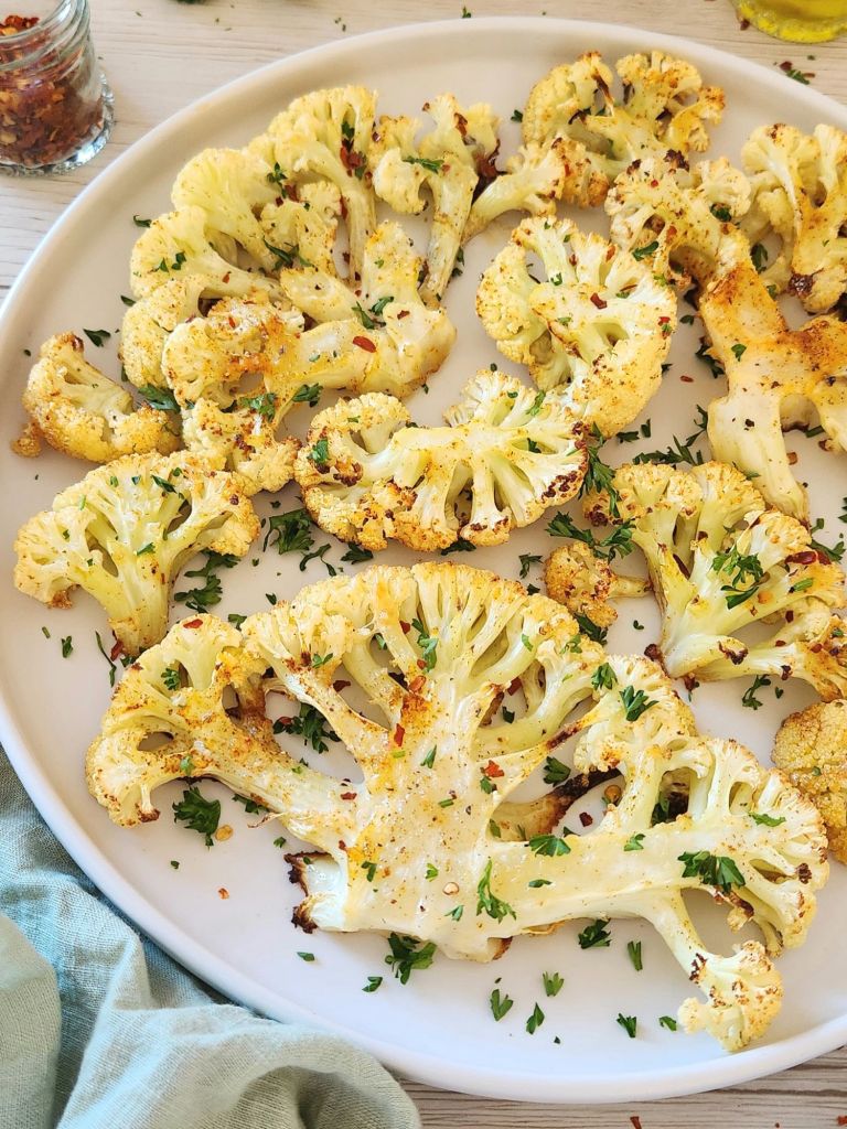 Golden roasted cauliflower with parmesan topped with fresh parsley on a white plate