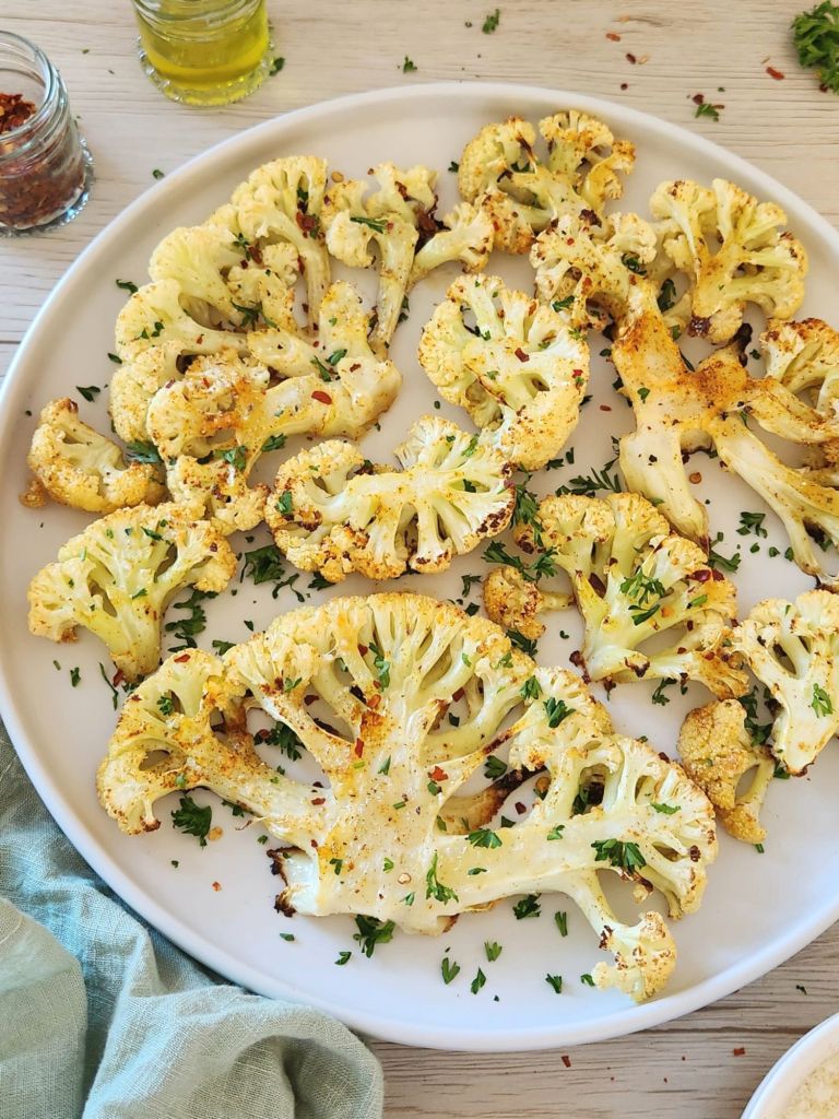 Golden roasted cauliflower with parmesan topped with fresh parsley on a white plate