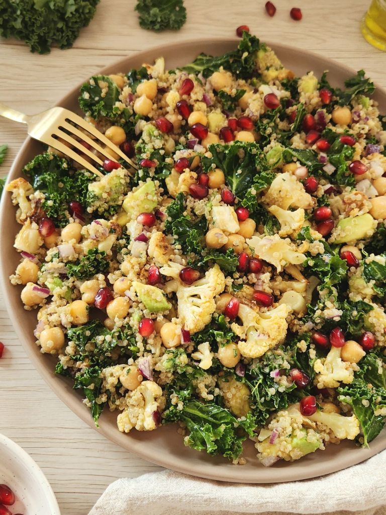 Healthy roasted cauliflower kale quinoa salad with chickpeas, avocado, tahini dressing, and pomegranate seeds in a rustic bowl.