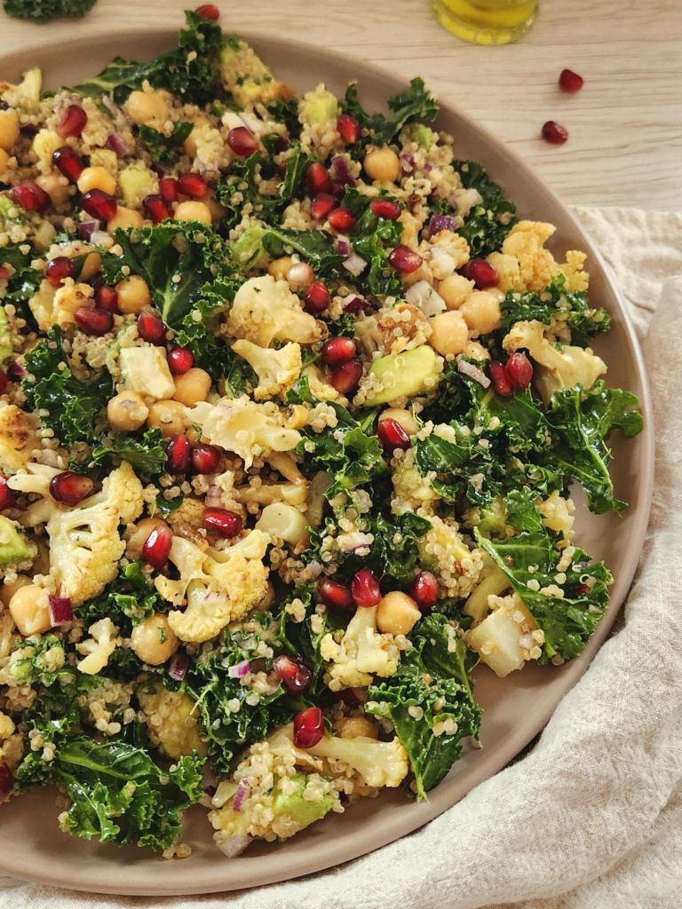 Healthy roasted cauliflower kale quinoa salad with chickpeas, avocado, tahini dressing, and pomegranate seeds in a rustic bowl.