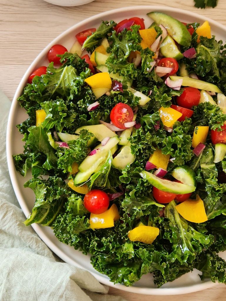 Fresh kale salad with chopped cucumber, cherry tomatoes, yellow bell pepper, red onion served in a white plate