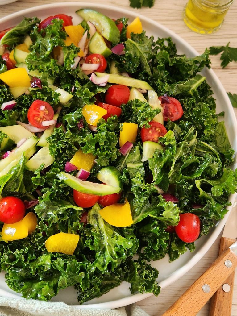 Fresh kale salad with chopped cucumber, cherry tomatoes, yellow bell pepper, red onion served in a white plate