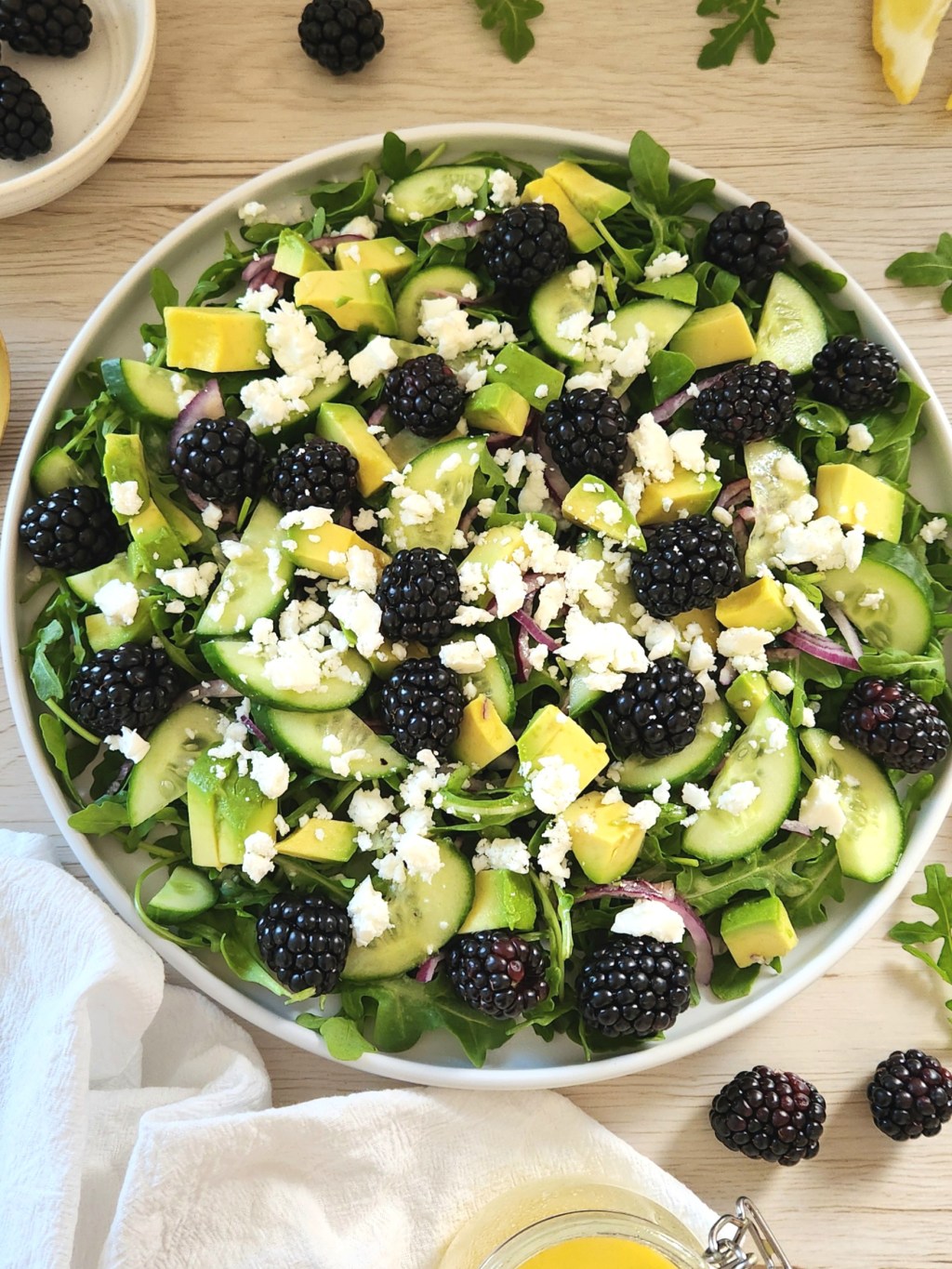 Fresh salad with blackberries, arugula, avocado, cucumber slices and crumbled feta served in a white plate
