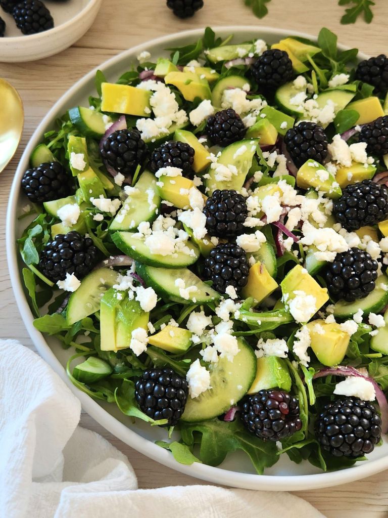 Fresh salad with blackberries, arugula, avocado, cucumber slices and crumbled feta served in a white plate