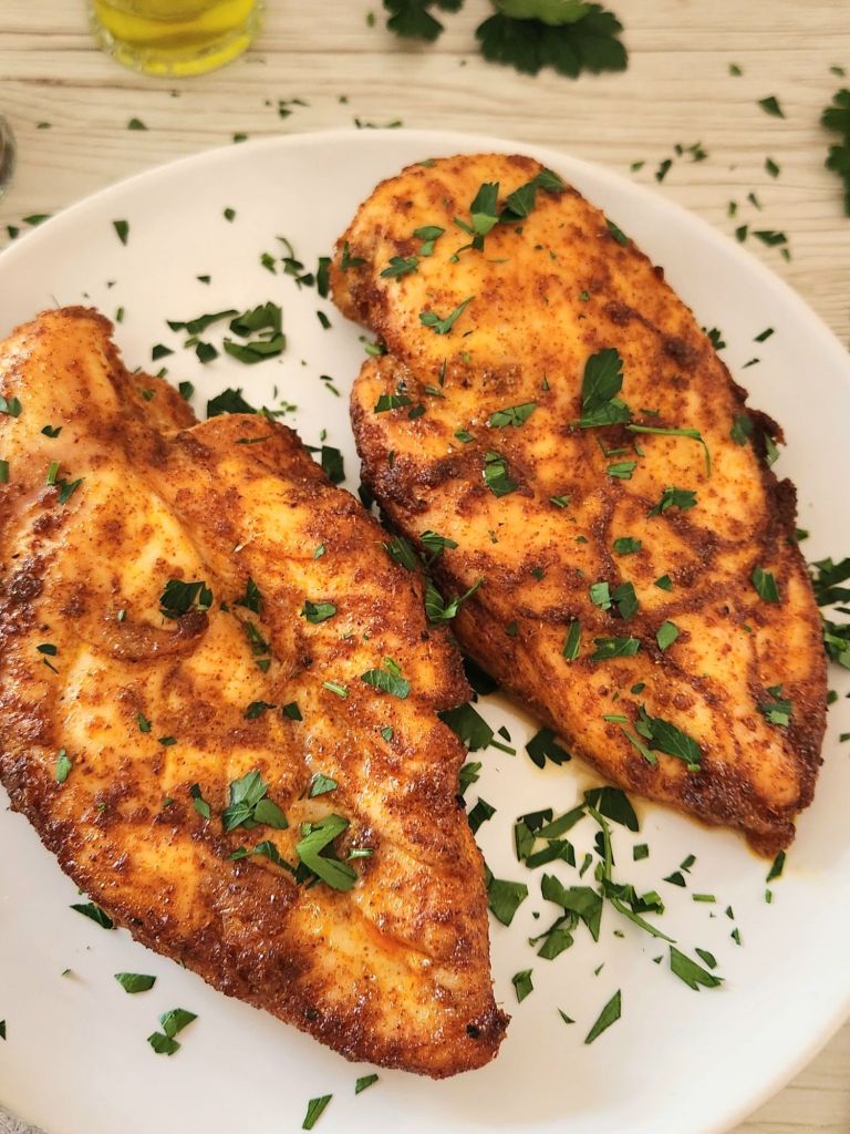 golden baked chicken breasts topped with fresh parsley and served on a white plate