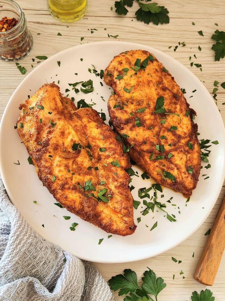 golden baked chicken breasts topped with fresh parsley and served on a white plate