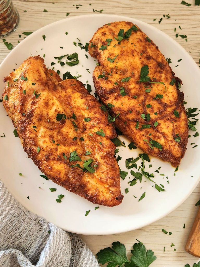 golden baked chicken breasts topped with fresh parsley and served on a white plate