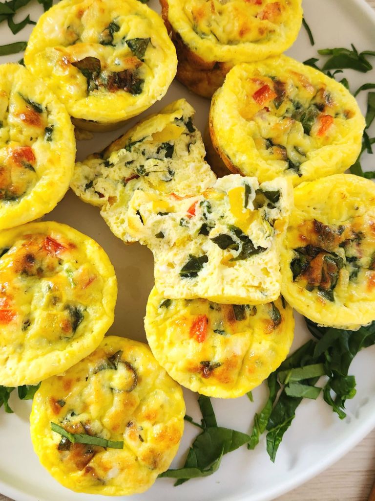 Healthy spinach feta Egg Muffins on a white plate with one muffin broken in half to show texture
