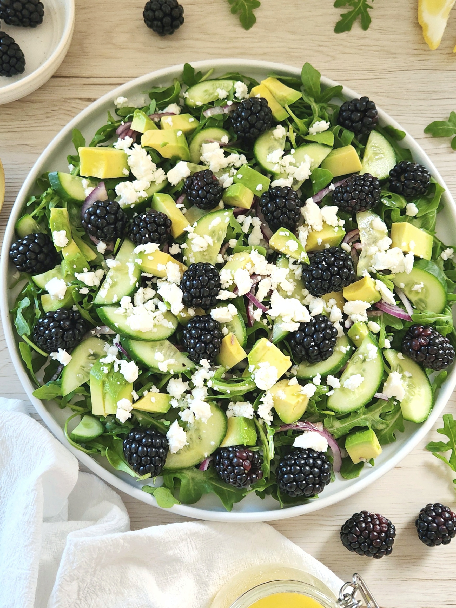 Fresh blackberry arugula avocado salad with cucumber slices and crumbled feta served in a white plate