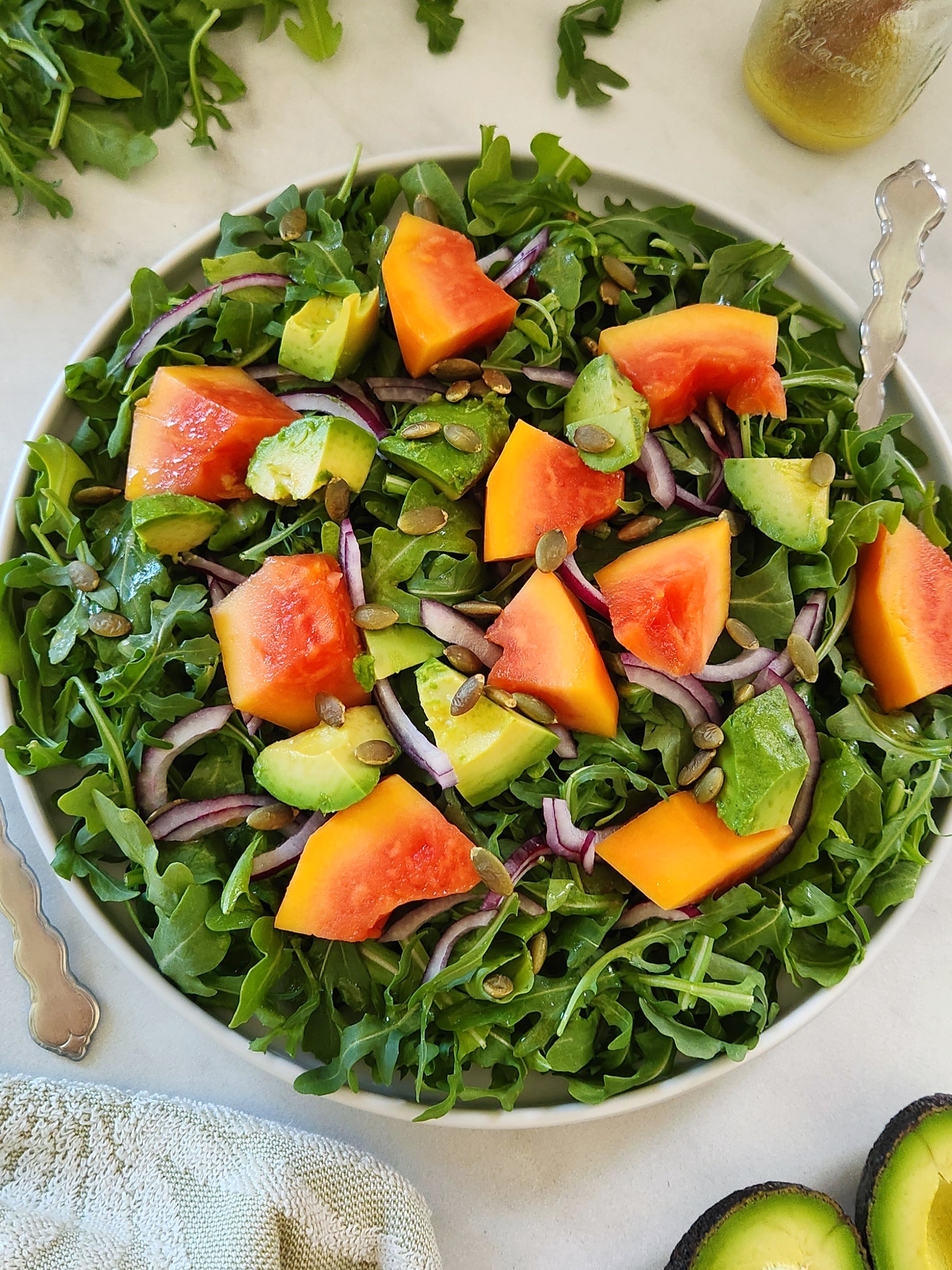 Fresh arugula papaya avocado salad with toasted pumpkin seeds and lime dressing served in a white plate