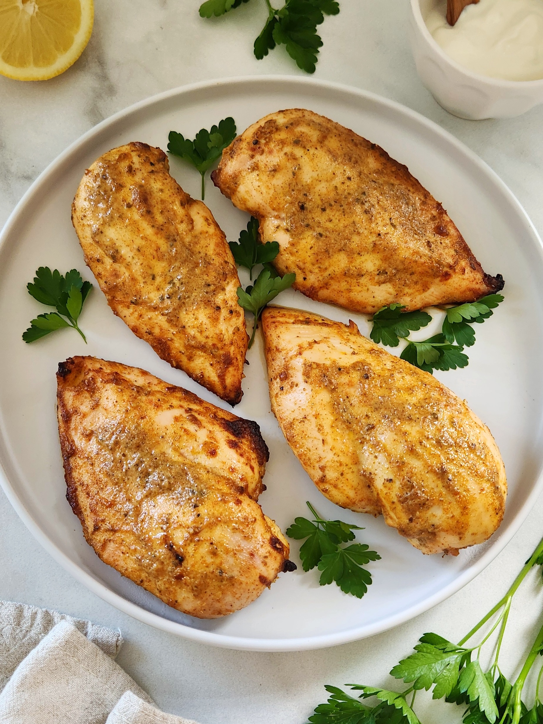 Greek yogurt baked chicken breast on a white plate with fresh parsley and cooked until golden and juicy