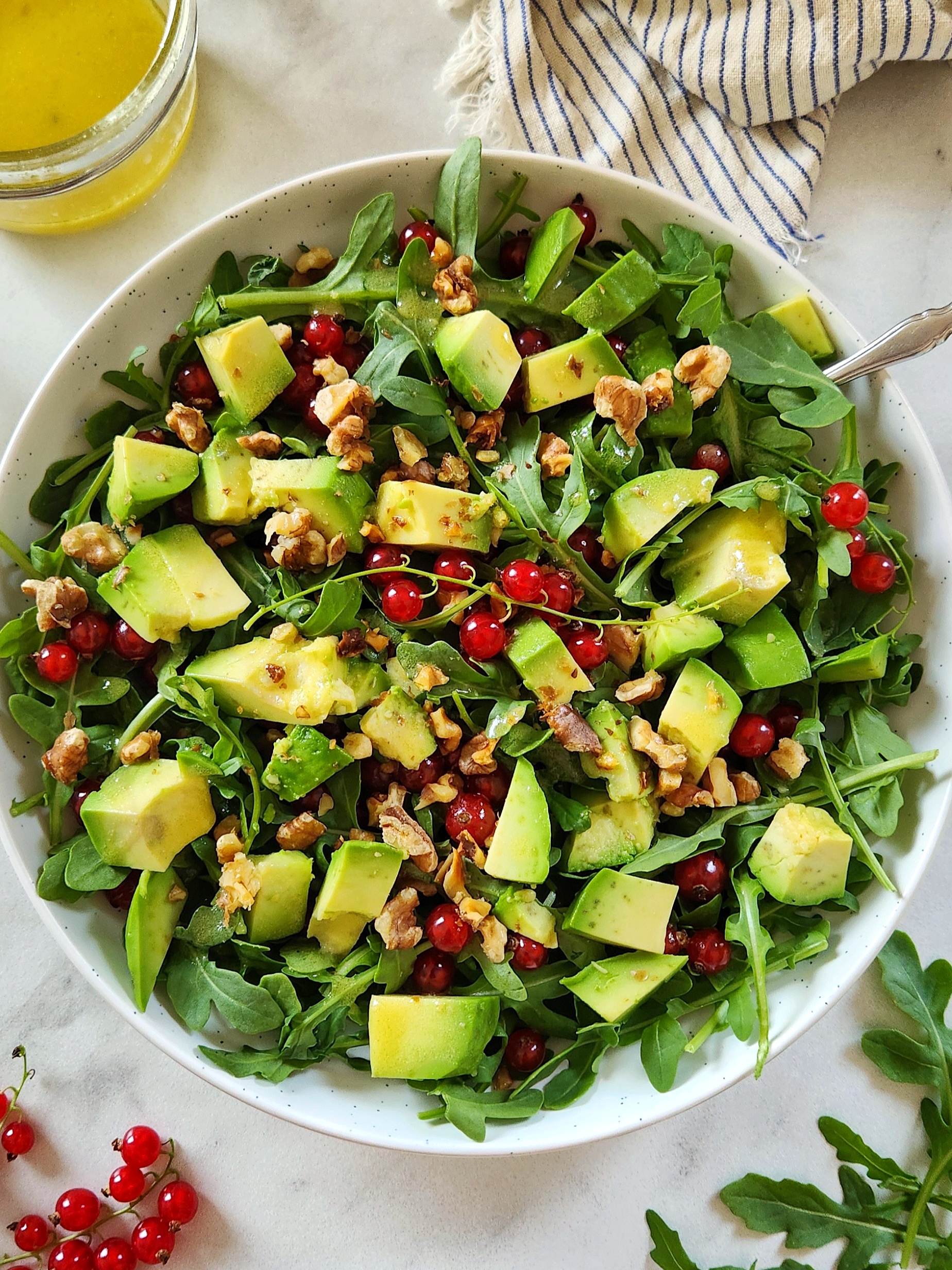 Fresh arugula avocado red currant salad with toasted walnuts and a lemon dressing served in a white bowl