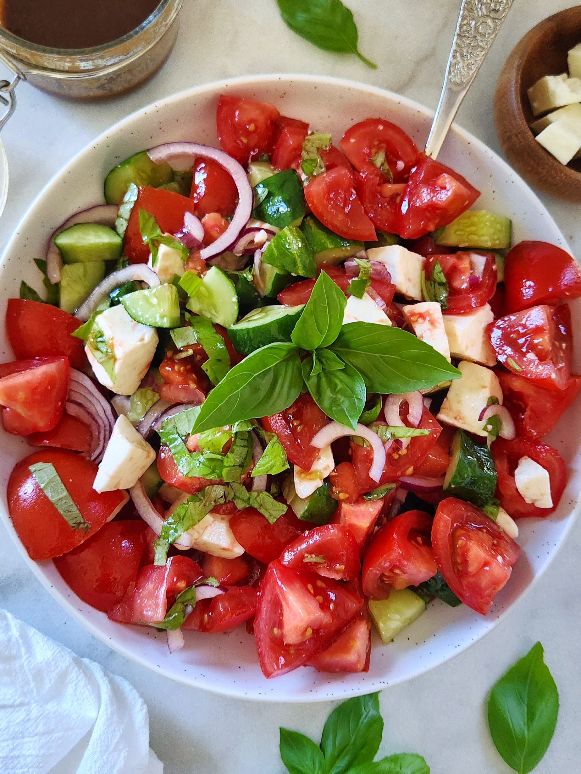 Fresh tomato cucumber feta salad with red onion, basil, and balsamic dressing in a white serving bowl.