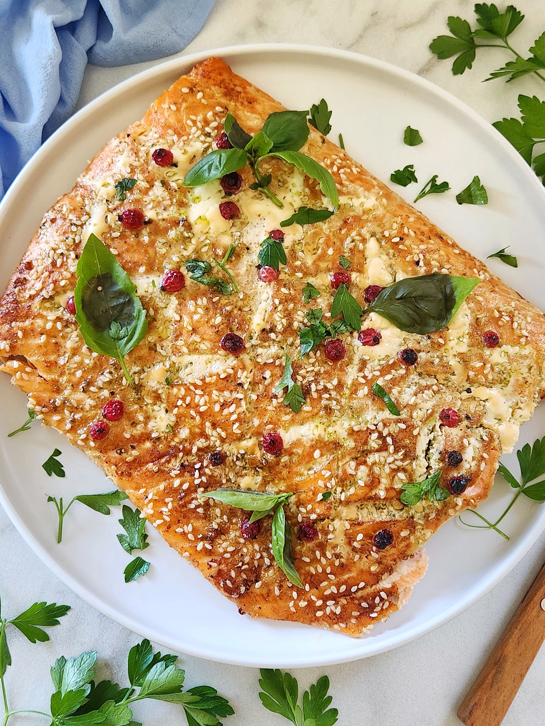 Baked salmon with pesto, sesame seeds, fresh basil, and red currants served on a white plate
